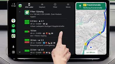 Android Auto Display zeigt Charging Time Ladeplanung mit Preisvergleich und Kartenroute, Hand tippt auf Ladesaeulenliste.