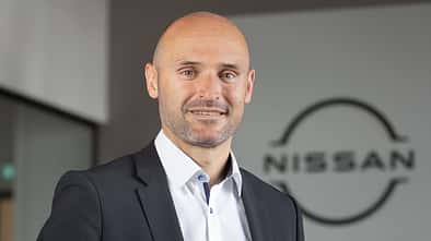 Pascal Michaeli von Nissan Deutschland steht in einem Bürogebäude vor einem Unternehmenslogo.