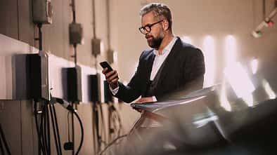 Mann bedient mit einem Smartphone den Ladevorgang eines Elektroautos an einer Wallbox in einer Tiefgarage