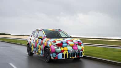 Skoda Epiq Elektro-SUV in Frontansicht mit Tarnfolierung auf nasser Landstraße bei bewölktem Himmel.