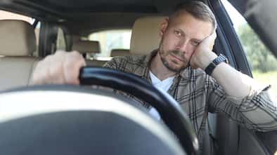 Arbeitnehmer sitzt im Fahrersitz eines Pkw und lehnt den Kopf an die Hand, Blick nach vorn, Innenraum eines Fahrzeugs.