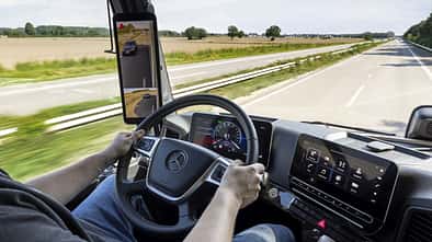 Blick aus dem Cockpit eines Mercedes-Lkw auf Straße, Display und digitale Spiegelanzeige während der Fahrt.