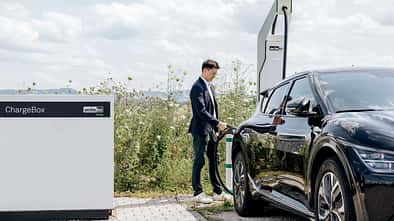 Person lädt ein Elektroauto an einer ChargeBox von ADS-TEC Energy im Außenbereich.