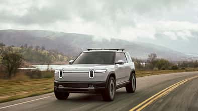 Rivian R2 in heller Lackierung auf einer Landstraße mit Berglandschaft im Hintergrund.