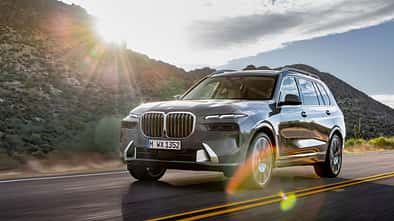 BMW X7 SUV in grauer Lackierung bei einer Fahrt auf einer Landstraße mit Berglandschaft im Hintergrund.