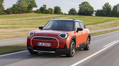 Orangefarbener Mini Aceman SE in Front-Dreiviertelansicht während der Fahrt auf einer Landstraße.