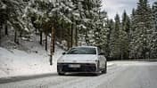 Hyundai Ioniq 6 frontal auf verschneiter Landstraße im Wald, Winterwetter, Fahrbahn mit Schneeresten.