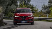 Roter Alfa Romeo Tonale in Fahrt, Frontansicht auf kurviger Straße mit Leitplanke und Bäumen im Hintergrund.