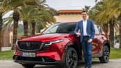 Felix Gebhart, Vertriebschef von Mazda Deutschland, steht neben einem roten Mazda CX-5 im Außenbereich.