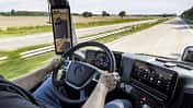 Blick aus dem Cockpit eines Mercedes-Lkw auf Straße, Display und digitale Spiegelanzeige während der Fahrt.