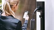 Eine Person bedient eine App vor einer Wallbox zum Laden eines Elektroautos am Wohnhaus.