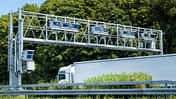Lkw fährt unter einer Mautbrücke auf einer europäischen Autobahn hindurch.