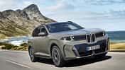 BMW iX xDrive60 in Frontansicht während der Fahrt auf einer Küstenstraße vor Berg- und Meereskulisse.