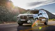 BMW X7 SUV in grauer Lackierung bei einer Fahrt auf einer Landstraße mit Berglandschaft im Hintergrund.
