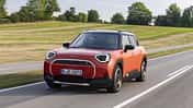 Orangefarbener Mini Aceman SE in Front-Dreiviertelansicht während der Fahrt auf einer Landstraße.
